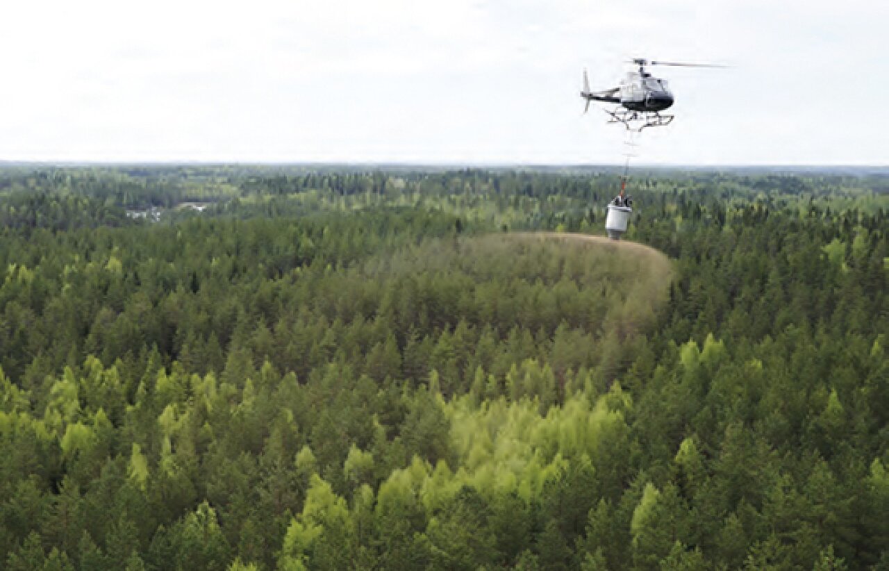Helikopter flyr over skogområde med gjødsel.